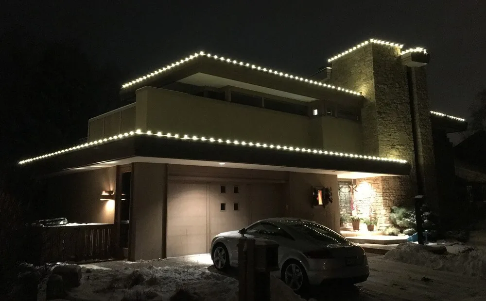 Modern flat-roofed home with warm white lights running the length of every roof edge and a lit stone entry