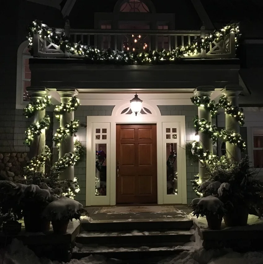 Covered entry detail with garland spiralling up both columns, a lit wreath and warm white eave lights