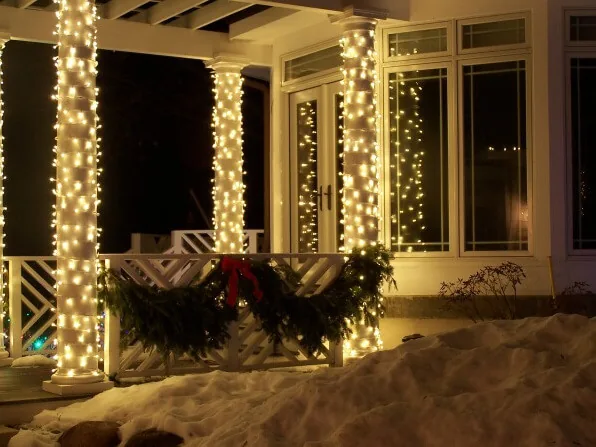 Porch detail of columns wrapped in warm white lights with lit garland along the railing and window frames
